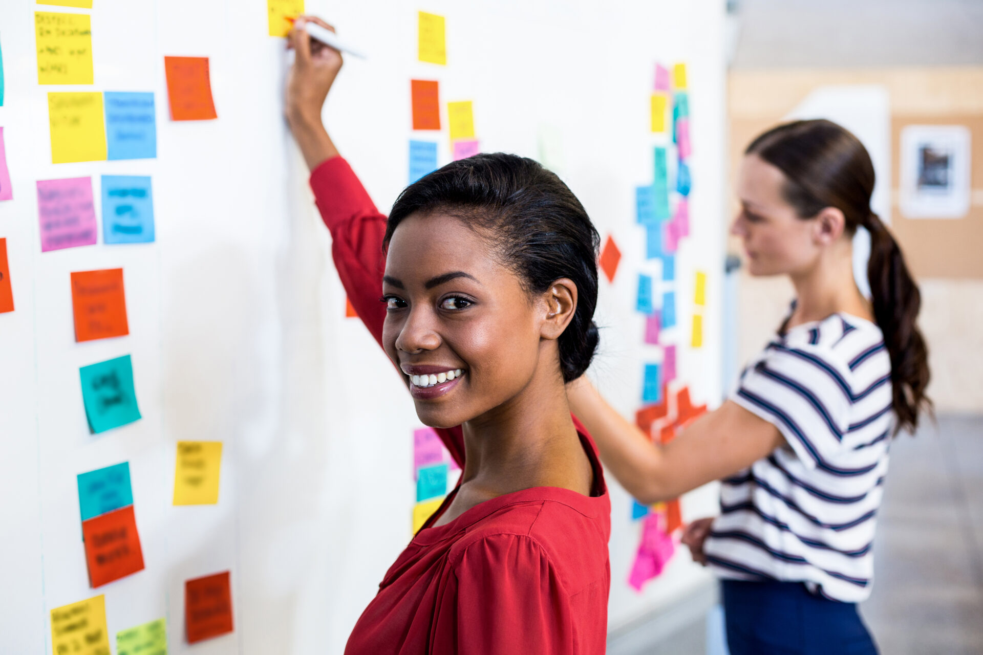 Young woman smiling at camera while writing on white board in the background